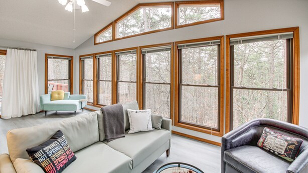 A spacious living room with a large window, a ceiling fan, and a sofa with decorative pillows. - 'stay and Play' - Hot Springs Village Home! (Hot Springs Village)