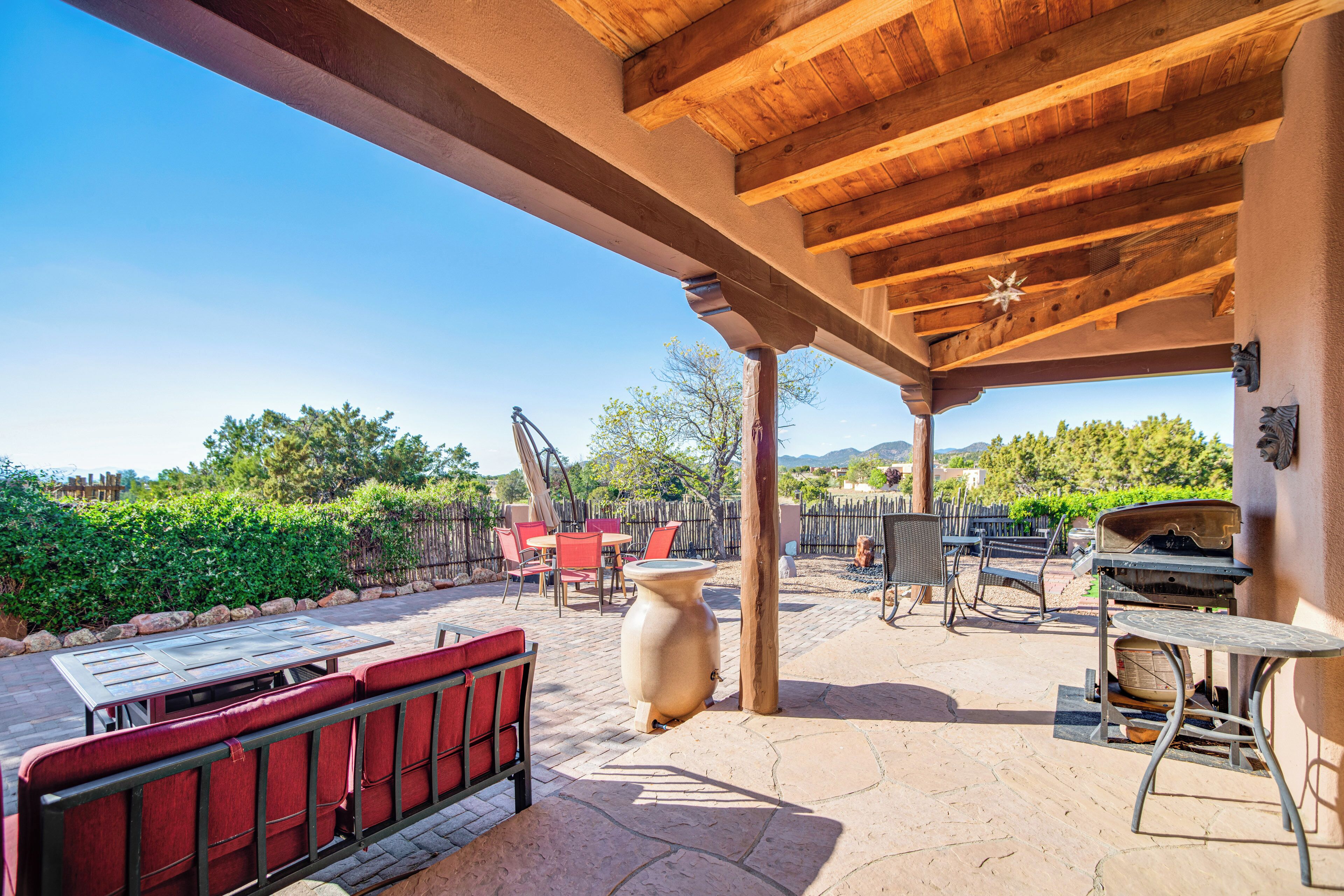 An outdoor patio with a wooden pergola, red cushioned seating, a large ceramic urn, and a grill.
