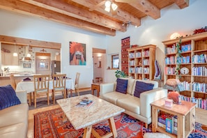 A cozy living room with a sofa, coffee table, and bookshelves filled with books. - Serene Santa Fe Getaway w/ Hot Tub & Fireplace! (Santa Fe)