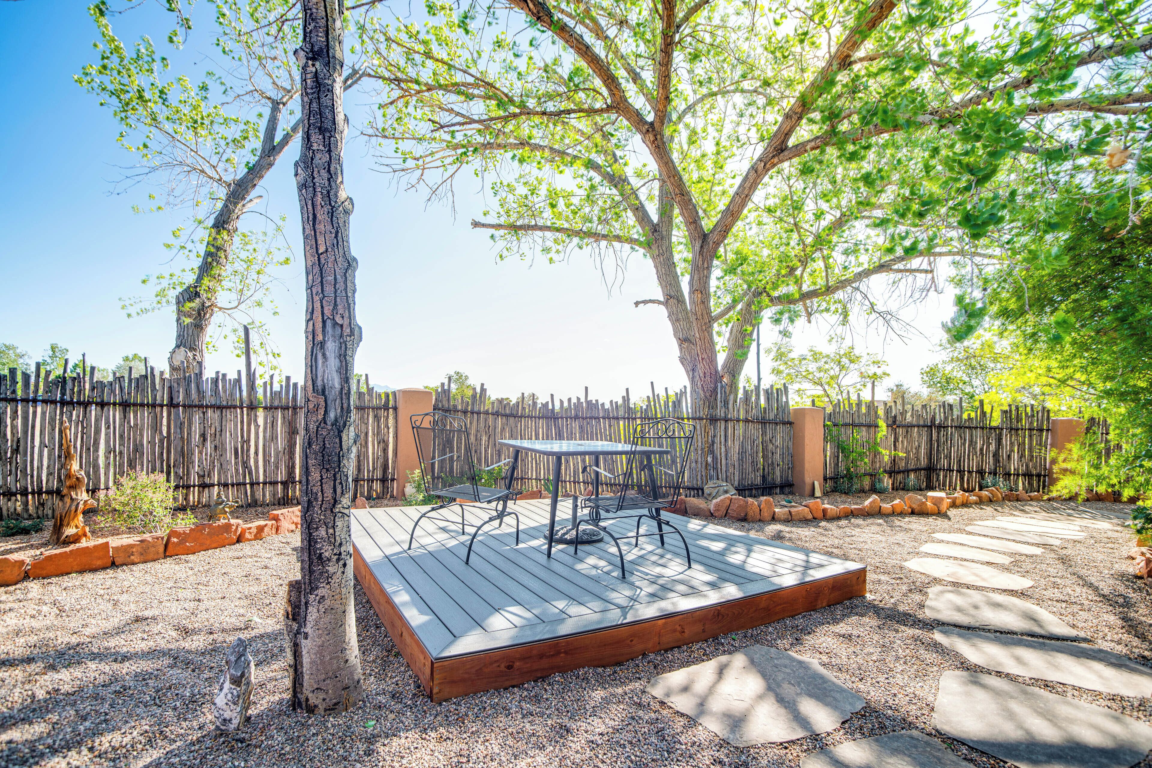 Une terrasse extérieure dotée d’une plateforme en bois, d’une table et de chaises en métal, entourée d’une zone recouverte de gravier et d’une clôture en bois.
