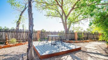 Une terrasse extérieure dotée d’une plateforme en bois, d’une table et de chaises en métal, entourée d’une zone recouverte de gravier et d’une clôture en bois.