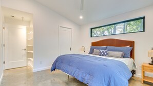 Una camera da letto con un letto grande, una finestra vista alberi, una ventola a soffitto e una porta che dà su un corridoio.