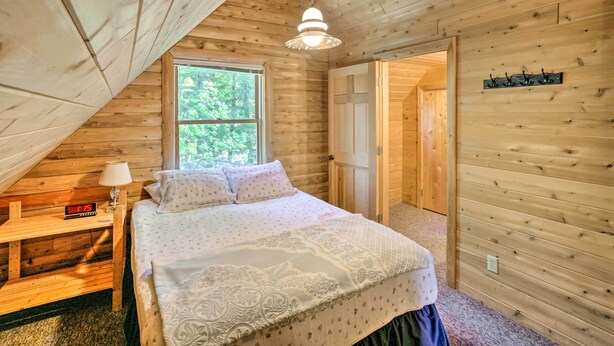 A wooden cabin bedroom with a bed, a nightstand with a lamp, a window, and a door. - Waterfront Lake Leelanau Log Cabin w/ Private Dock (Lake Leelanau)