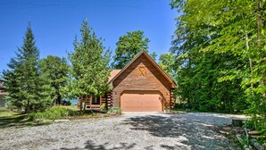 A log cabin with a garage, surrounded by trees and a gravel driveway. - Waterfront Lake Leelanau Log Cabin w/ Private Dock (Lake Leelanau)