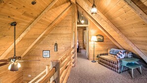 A cozy attic room with wooden beams, a plaid sofa, a small table, and a lamp. - Waterfront Lake Leelanau Log Cabin w/ Private Dock (Lake Leelanau)