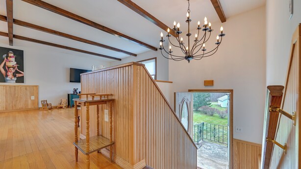 A spacious room with wooden floors, a staircase with wooden railings, a chandelier, and a view of the outdoors. - Vacation Rental Home ~ 2 Mi to Windham Mountain! (Windham)