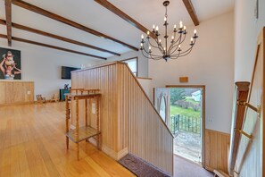 Amplia habitación con pisos de madera, una escalera con barandilla de madera, una araña y vistas al exterior.
