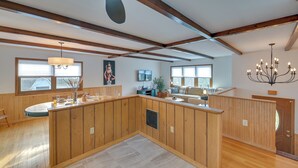 A spacious living area with wooden paneling, a central island with a sink, a chandelier, and a large window providing natural light. - Vacation Rental Home ~ 2 Mi to Windham Mountain! (Windham)