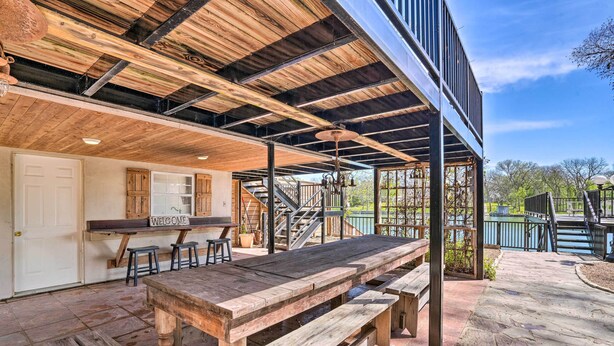 An outdoor patio with a wooden table and benches, a staircase leading to an upper level, and a 'Welcome' sign. - Guadalupe Riverfront Studio w/ Private Balcony (Seguin)