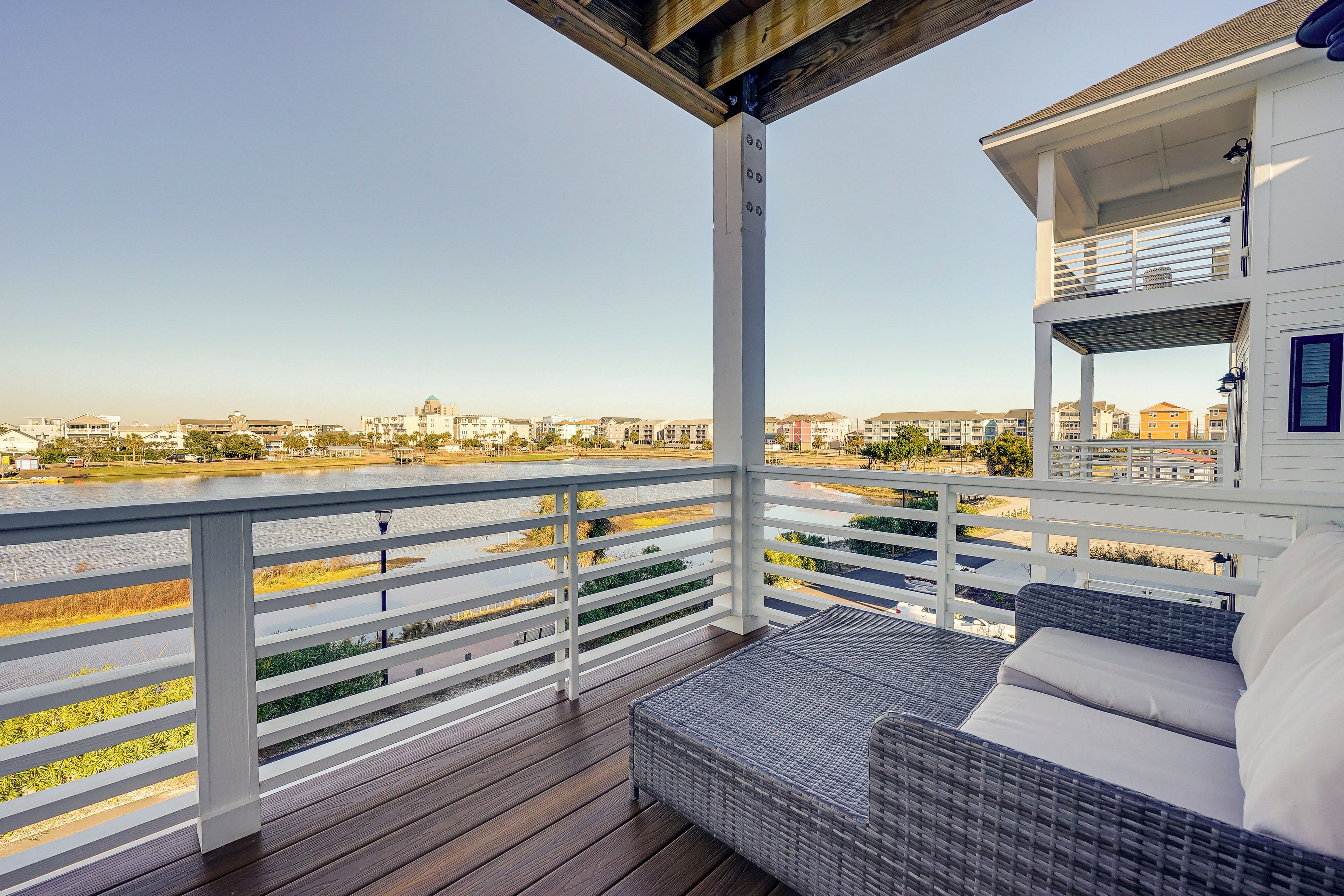 A balcony with a wicker sofa, a railing, and a view of a river and buildings.