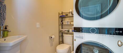 A compact bathroom with a sink, toilet, and stacked washer-dryer unit.