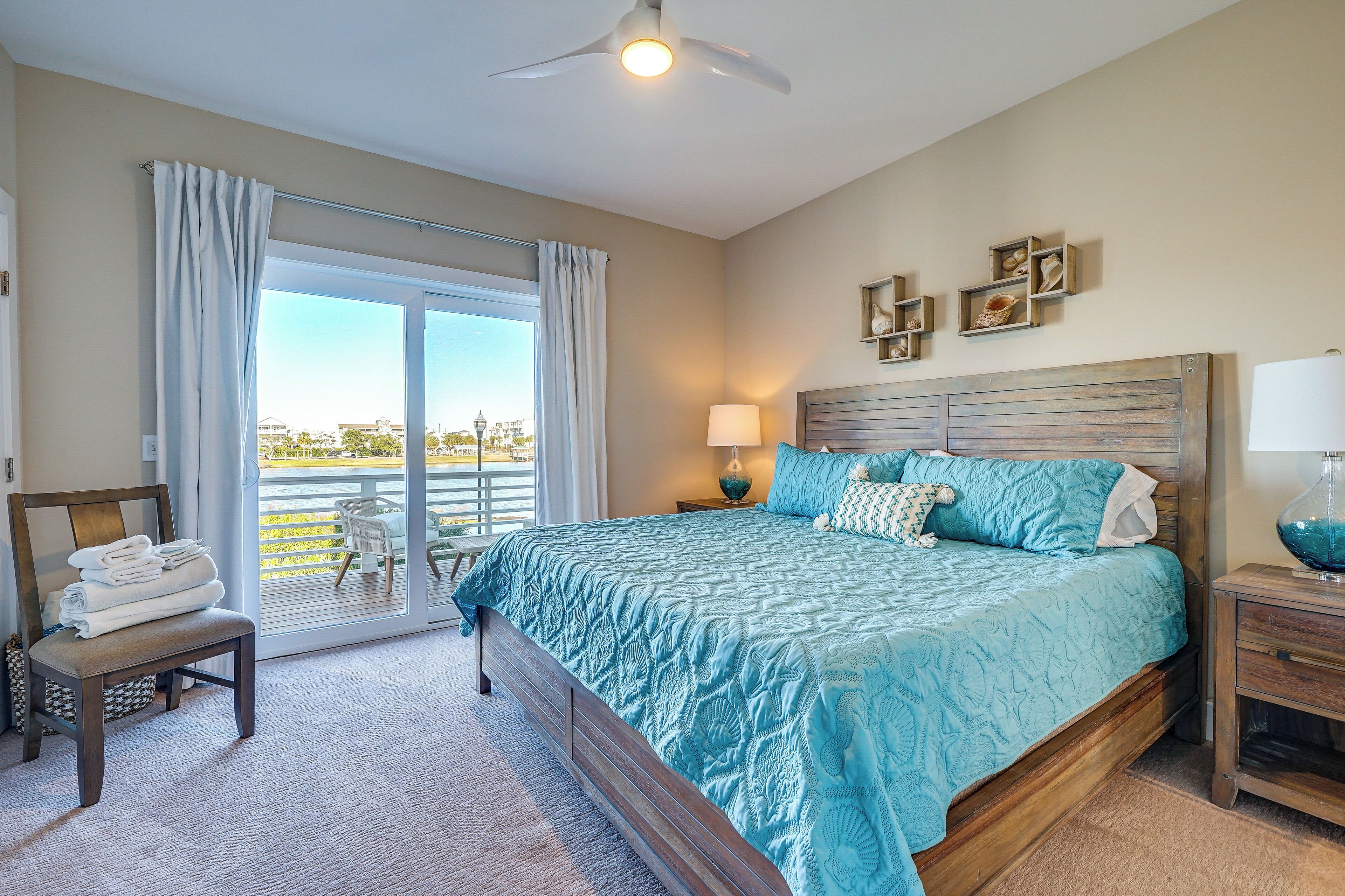 A bedroom with a large bed, a chair with towels, a nightstand with a lamp, and a view of the outdoors through a sliding door.