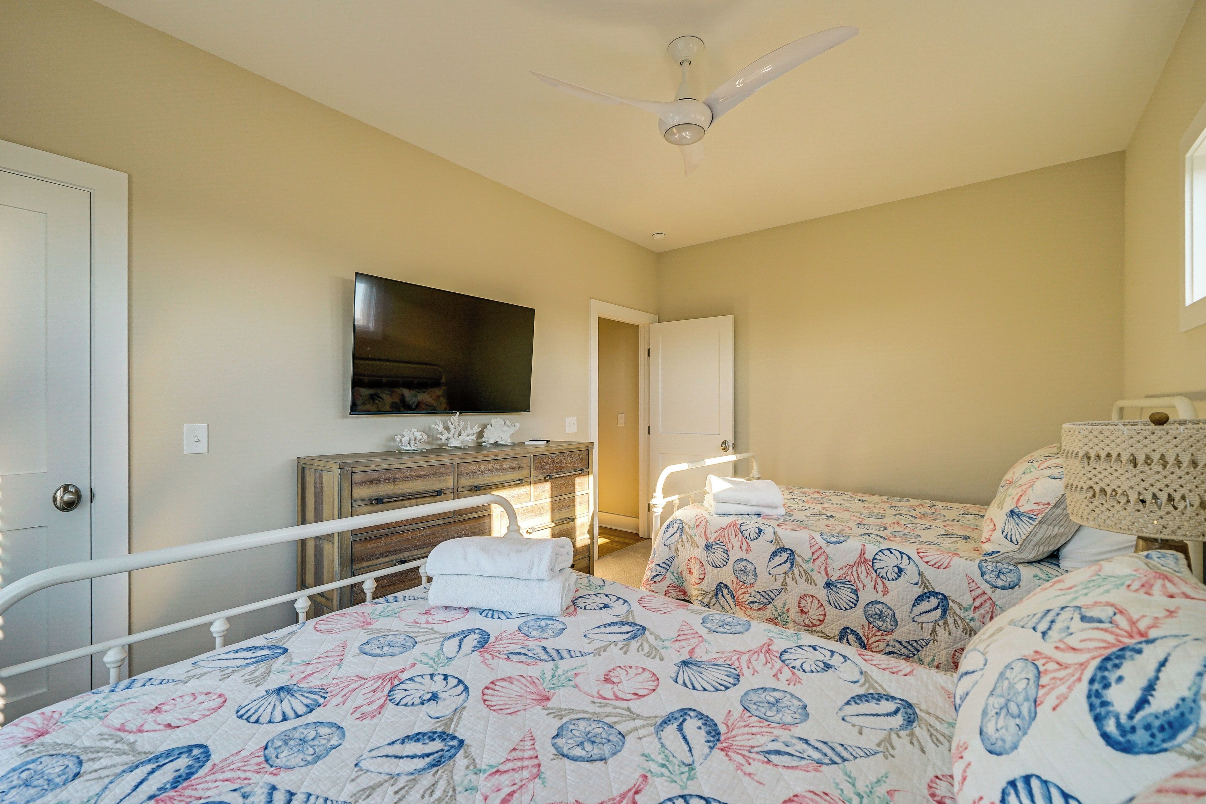 A bedroom with two beds, a television, a dresser, and a ceiling fan.