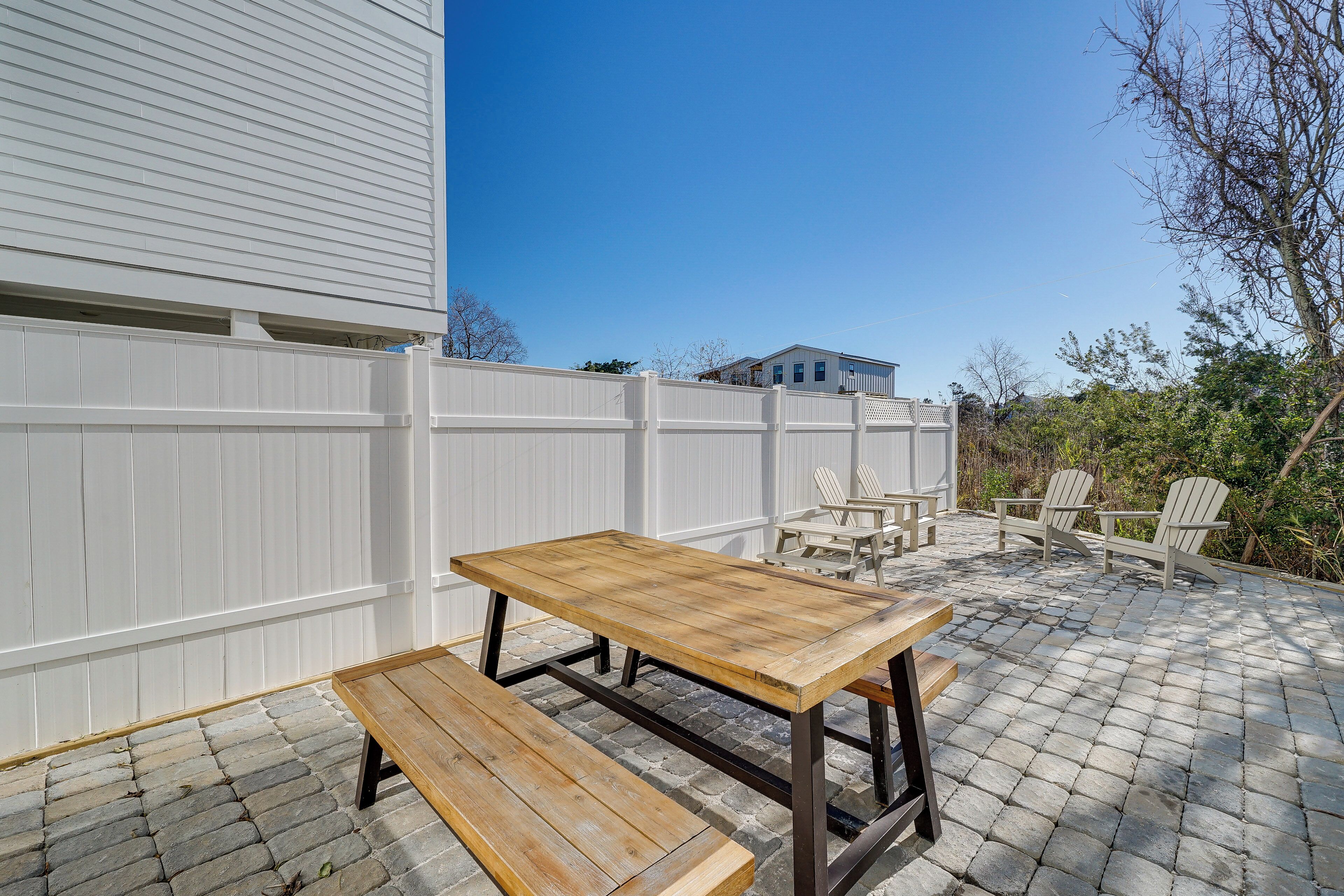 Eine Terrasse im Freien mit einem Holztisch und Bänken, umgeben von einem weißen Zaun und einem Pflasterboden.