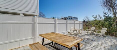 An outdoor patio with a wooden table and benches, surrounded by a white fence and a brick floor.