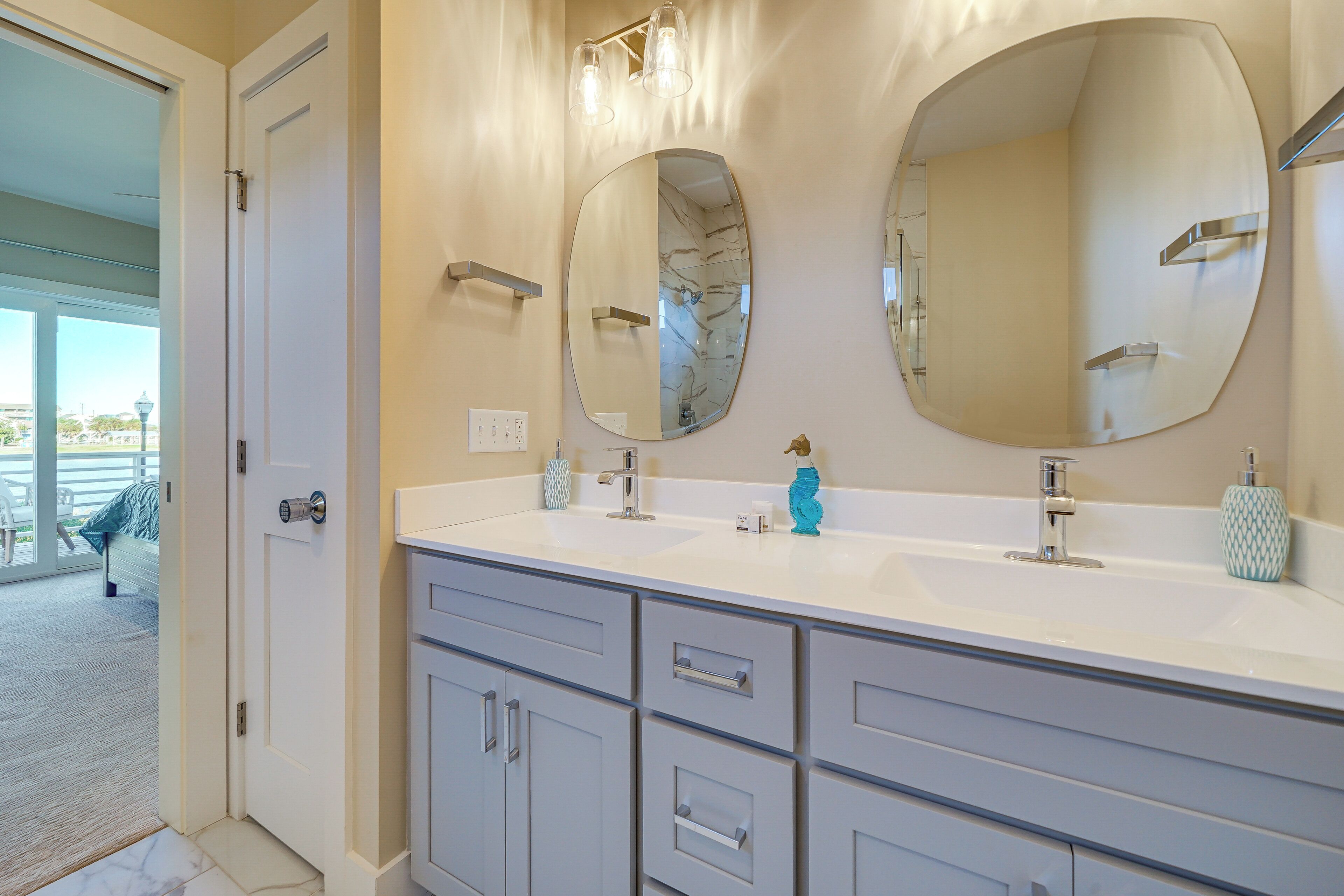 A bathroom with two large oval mirrors, a white sink, and grey cabinetry.