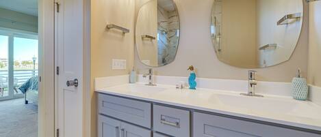 A bathroom with two large oval mirrors, a white sink, and grey cabinetry.