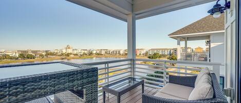 A balcony with wicker furniture, a glass table, and a view of a body of water and buildings.