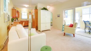 A spacious living room with a white sofa, a green stool, a white cabinet, and a dining area with a table and chairs. - Sunny Wells Cottage - 1 Mi to Moody Beach! (Wells)