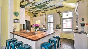 A kitchen with a wooden island, bar stools, and a refrigerator with a decorative magnet. - Historic Galveston Hideaway, Walk to the Beach! (Galveston)