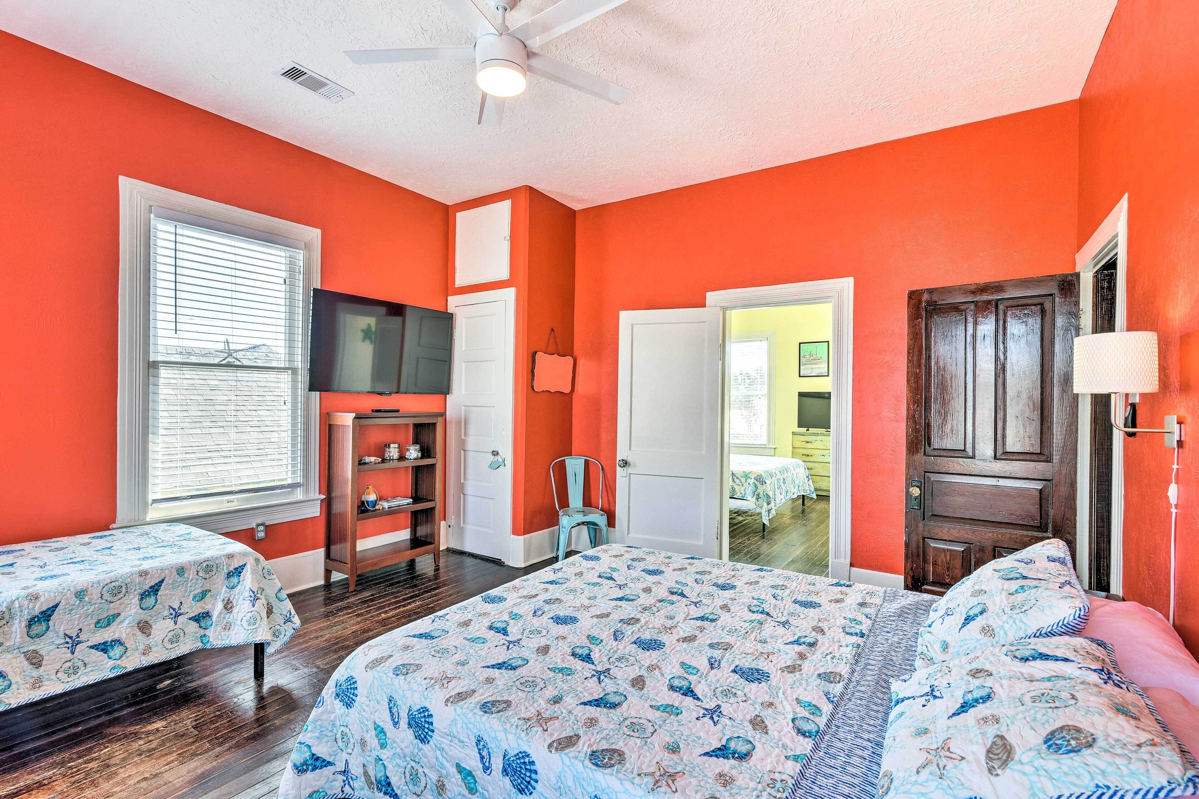 A bedroom with two beds, a ceiling fan, a window with blinds, a wooden door, and a small cabinet.