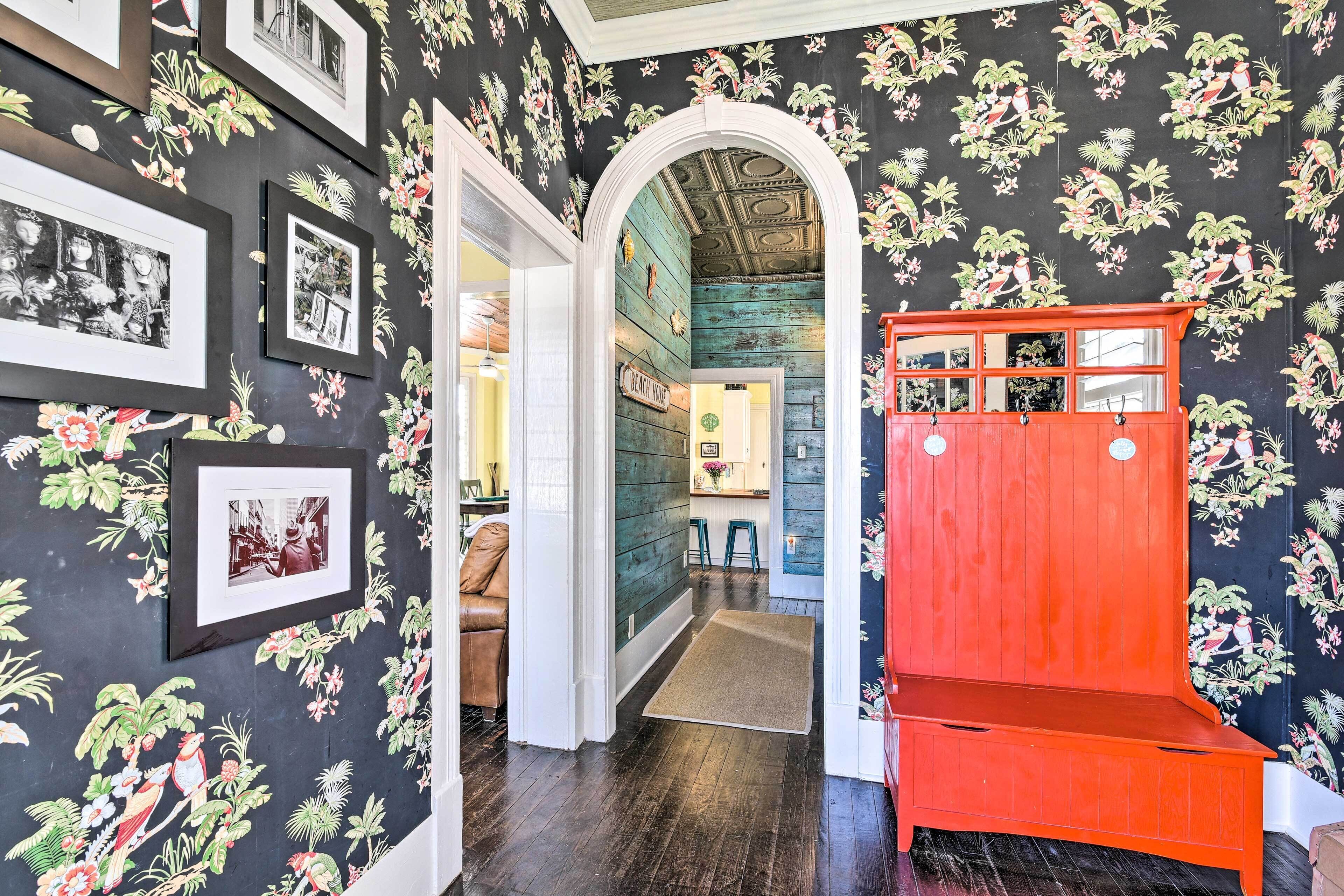 Un pasillo con pisos de madera oscura, un banco rojo y paredes cubiertas de papel tapiz floral.