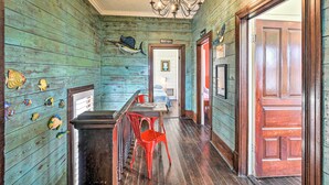 A rustic interior with wooden walls, a chandelier, a bar area with red chairs, and a wooden door. - Historic Galveston Hideaway, Walk to the Beach! (Galveston)