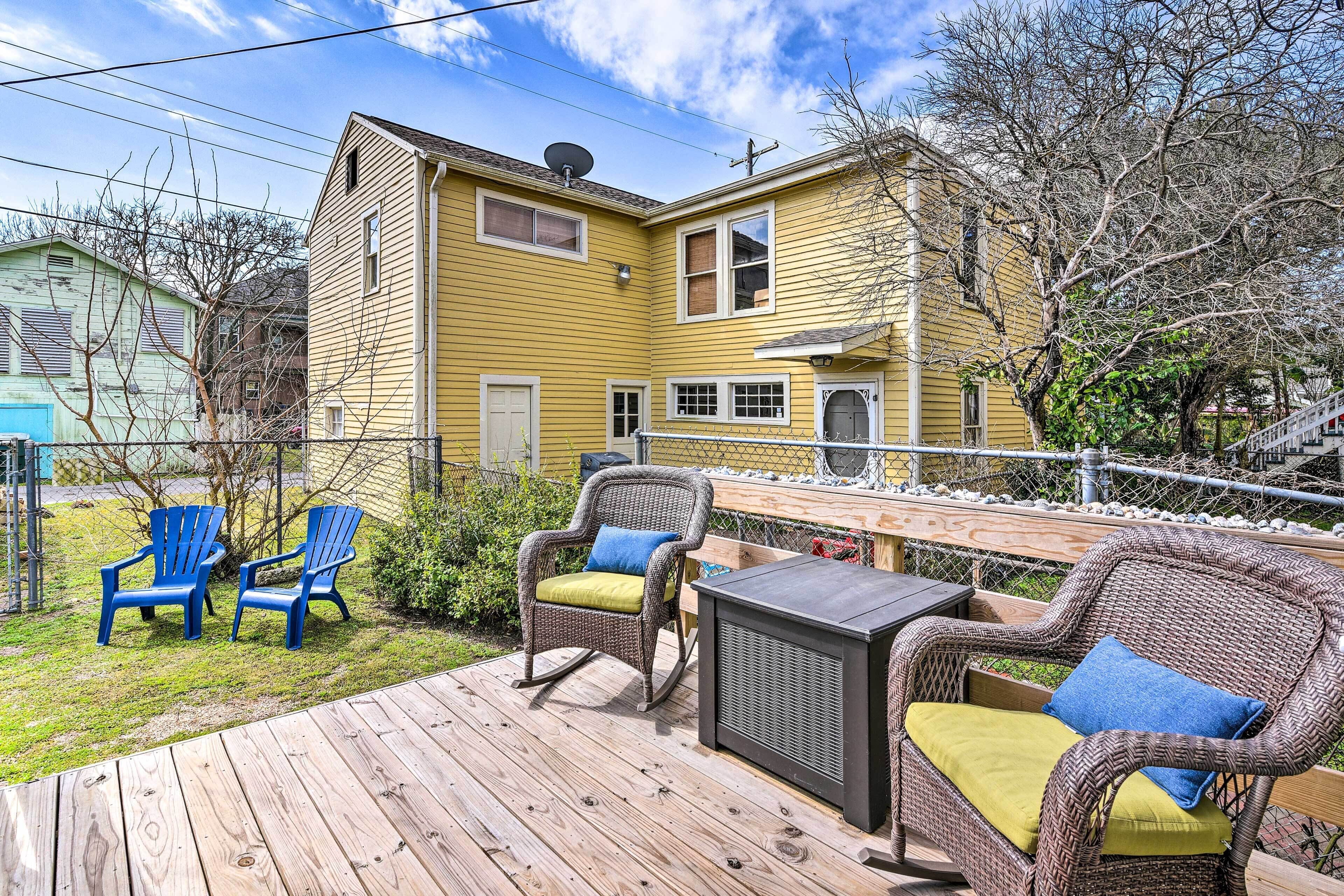 A yellow house with a deck, wicker furniture, and blue Adirondack chairs.