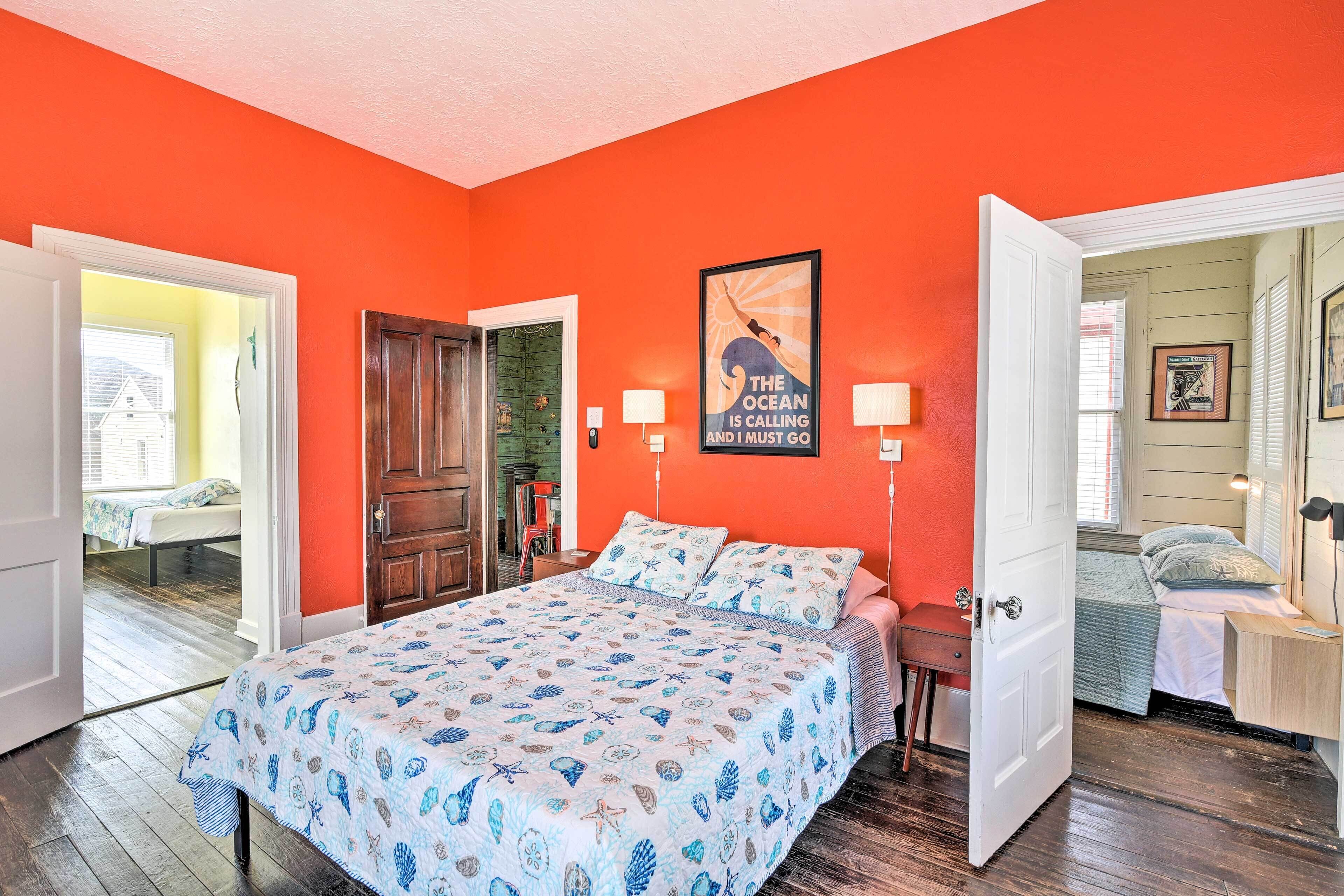 A room with a large bed, two bedside tables, and a door leading to another room.