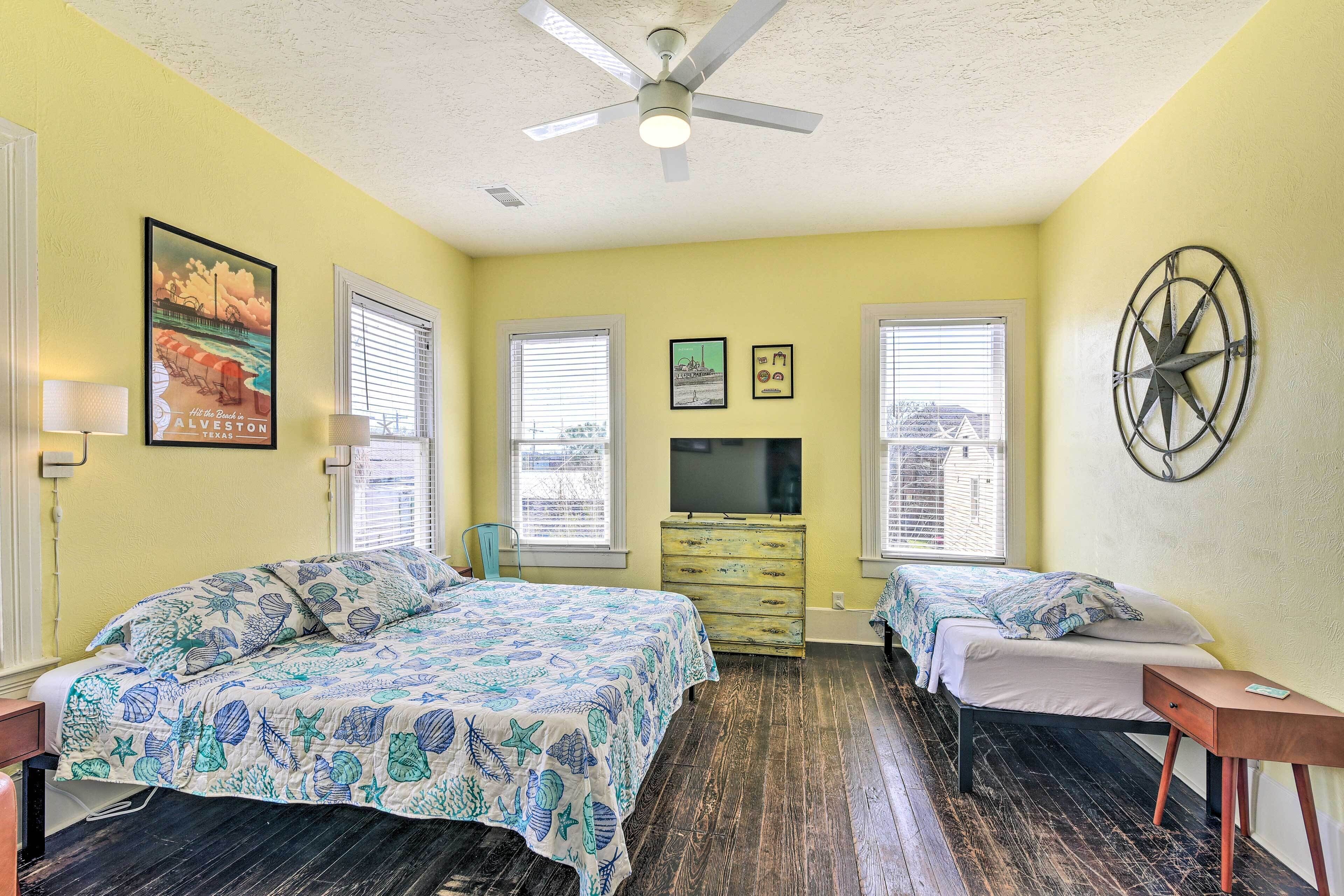 Une chambre avec deux lits, un ventilateur de plafond, une télévision et une commode.