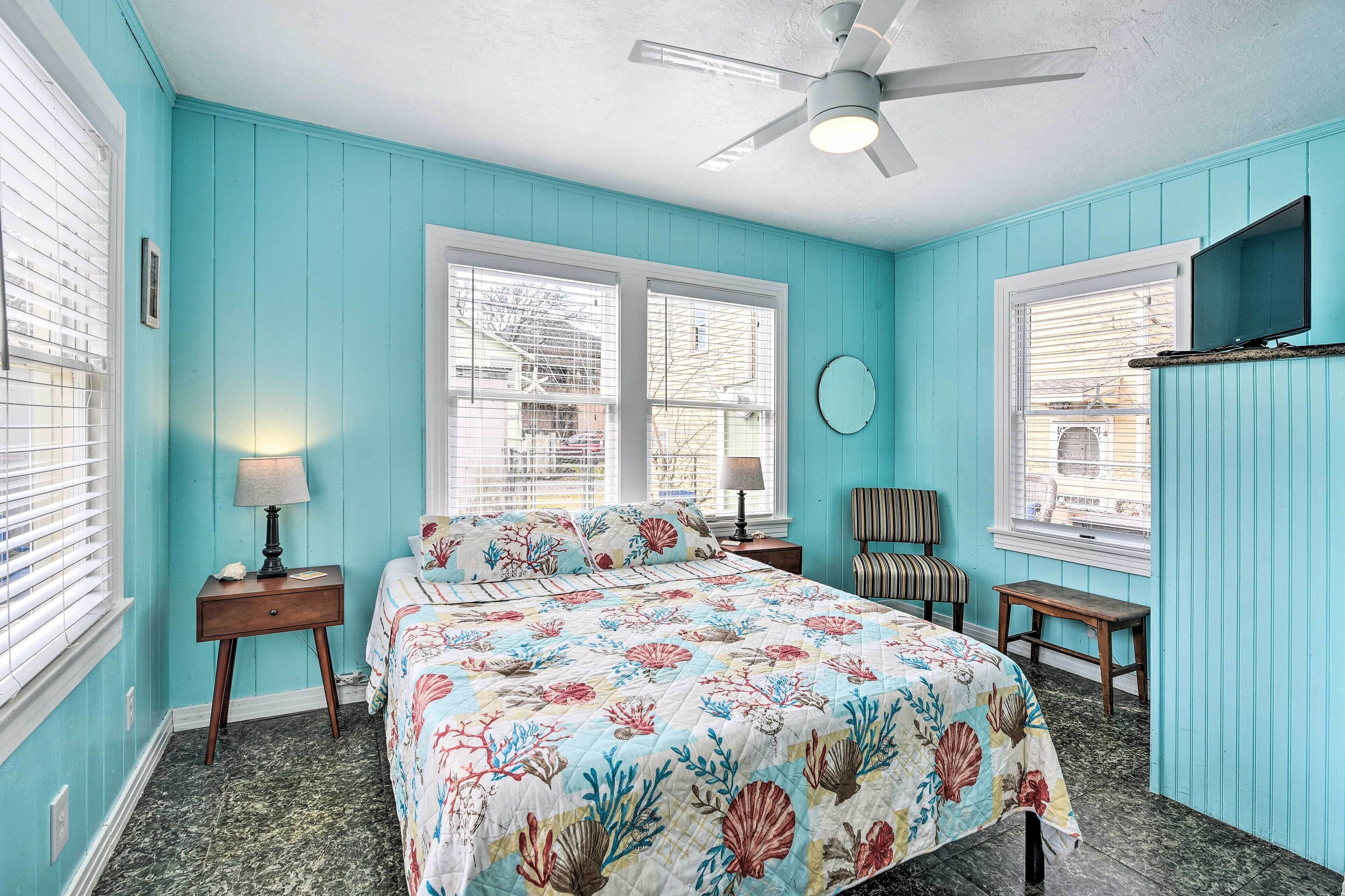 A bedroom with a bed, two nightstands, a chair, a ceiling fan, and a window with blinds.