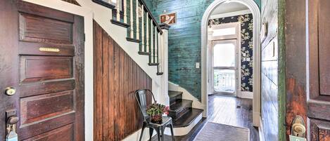 A wooden staircase with a handrail, a door labeled 'MERMAID,' and a rug leading to a door with a floral wallpaper.