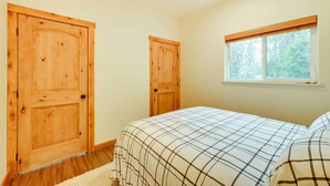 Une chambre à coucher avec deux portes en bois, une fenêtre donnant sur des arbres et un lit recouvert d’une couverture à carreaux.