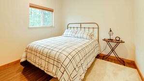 Un dormitorio con cama, ventana, mesita de noche con lámpara y alfombra.