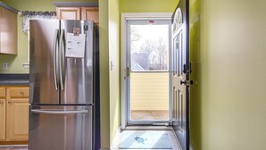 A kitchen with a stainless steel refrigerator, wooden cabinets, and a sliding glass door leading to a backyard.