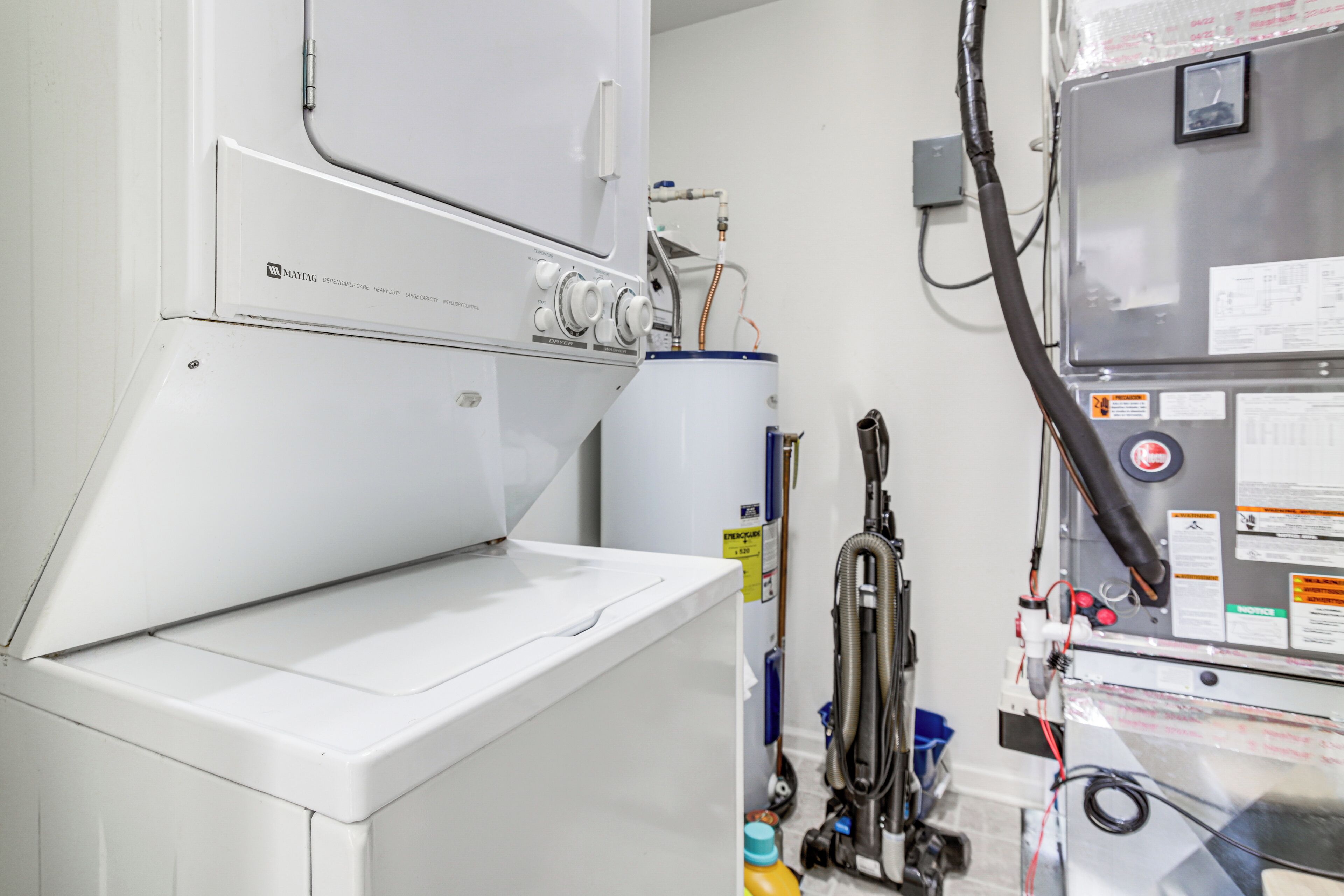 A laundry room with a white washing machine, a water heater, and various hoses and controls.