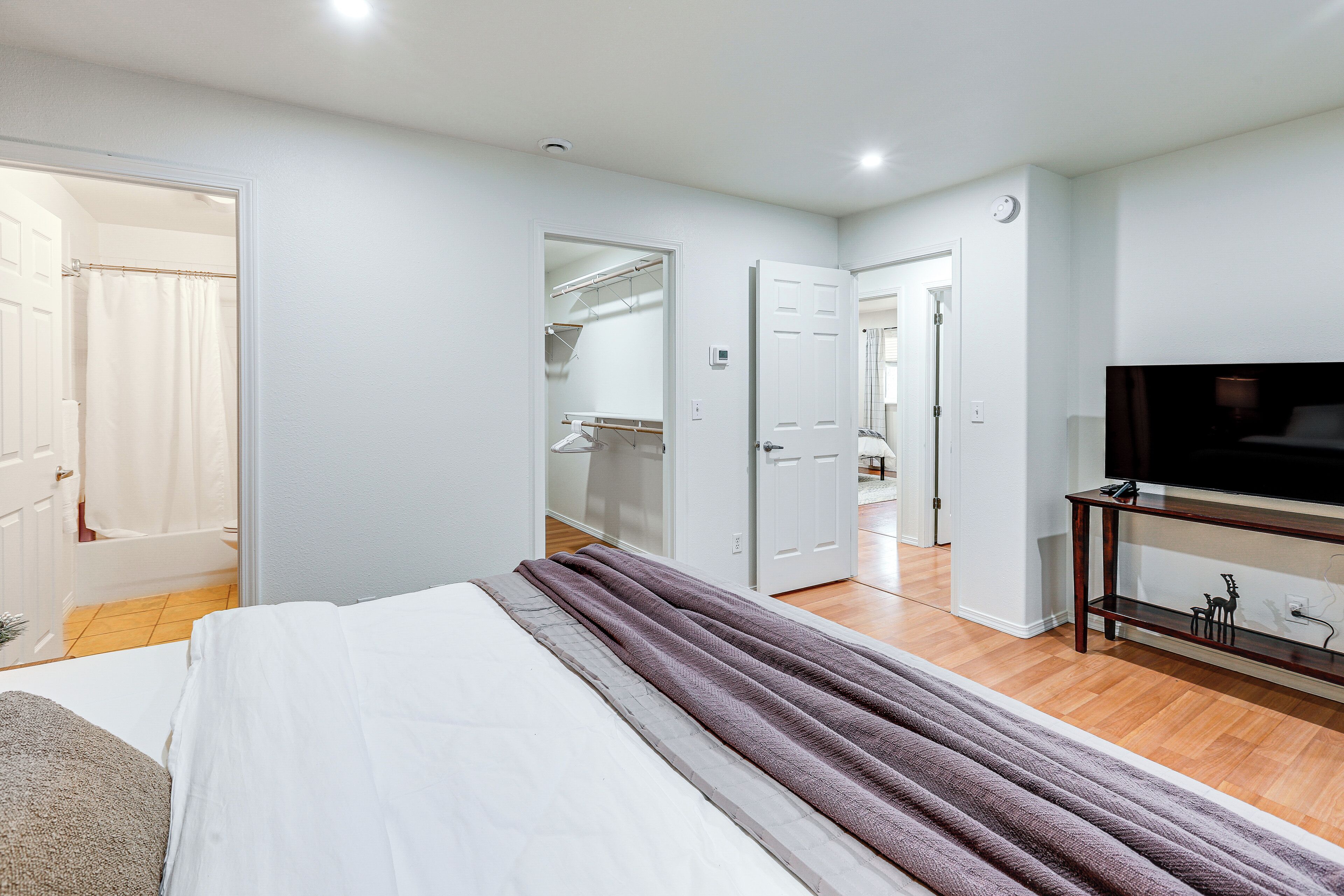 Une chambre à coucher avec un lit, une télévision, une armoire et une salle de bain visible à travers une porte ouverte.