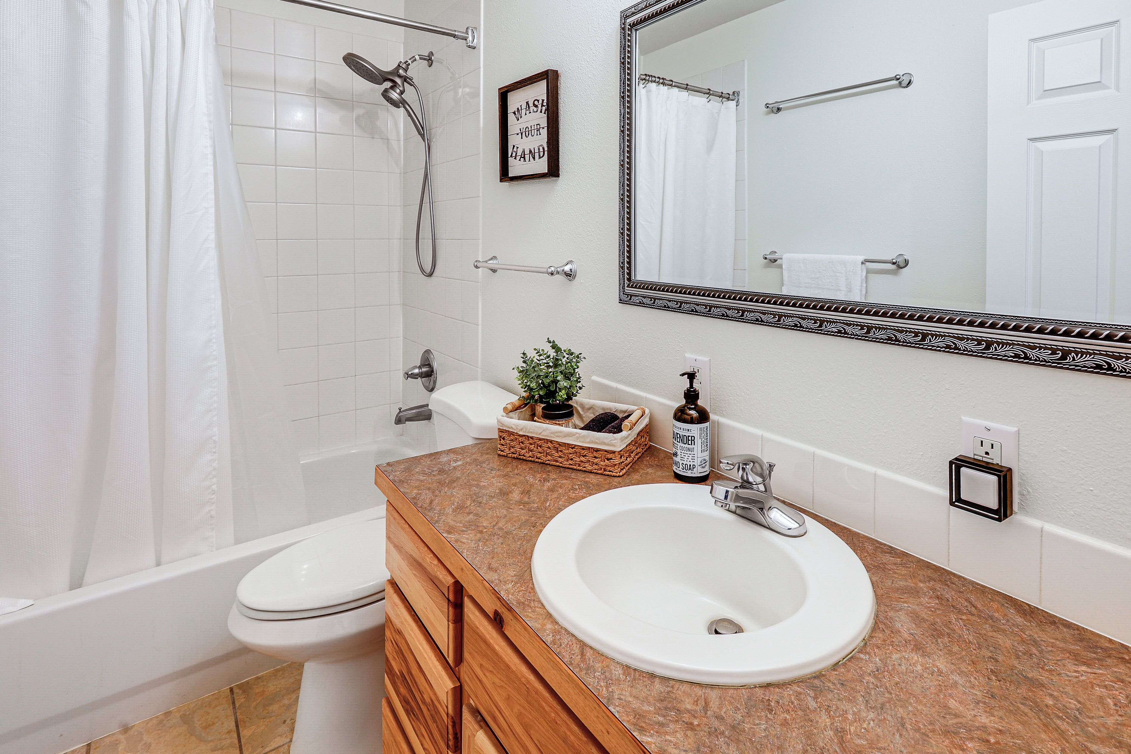 Un baño con inodoro blanco, lavamanos con encimera de mármol, espejo con marco decorativo, ducha con puerta de cristal y toallero.