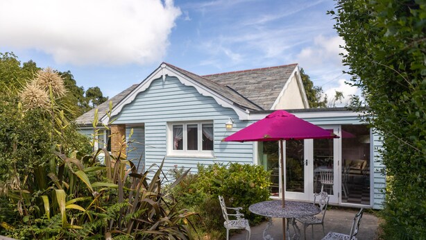 Une maison bleu clair avec un patio comprenant une table, des chaises et un parasol violet.