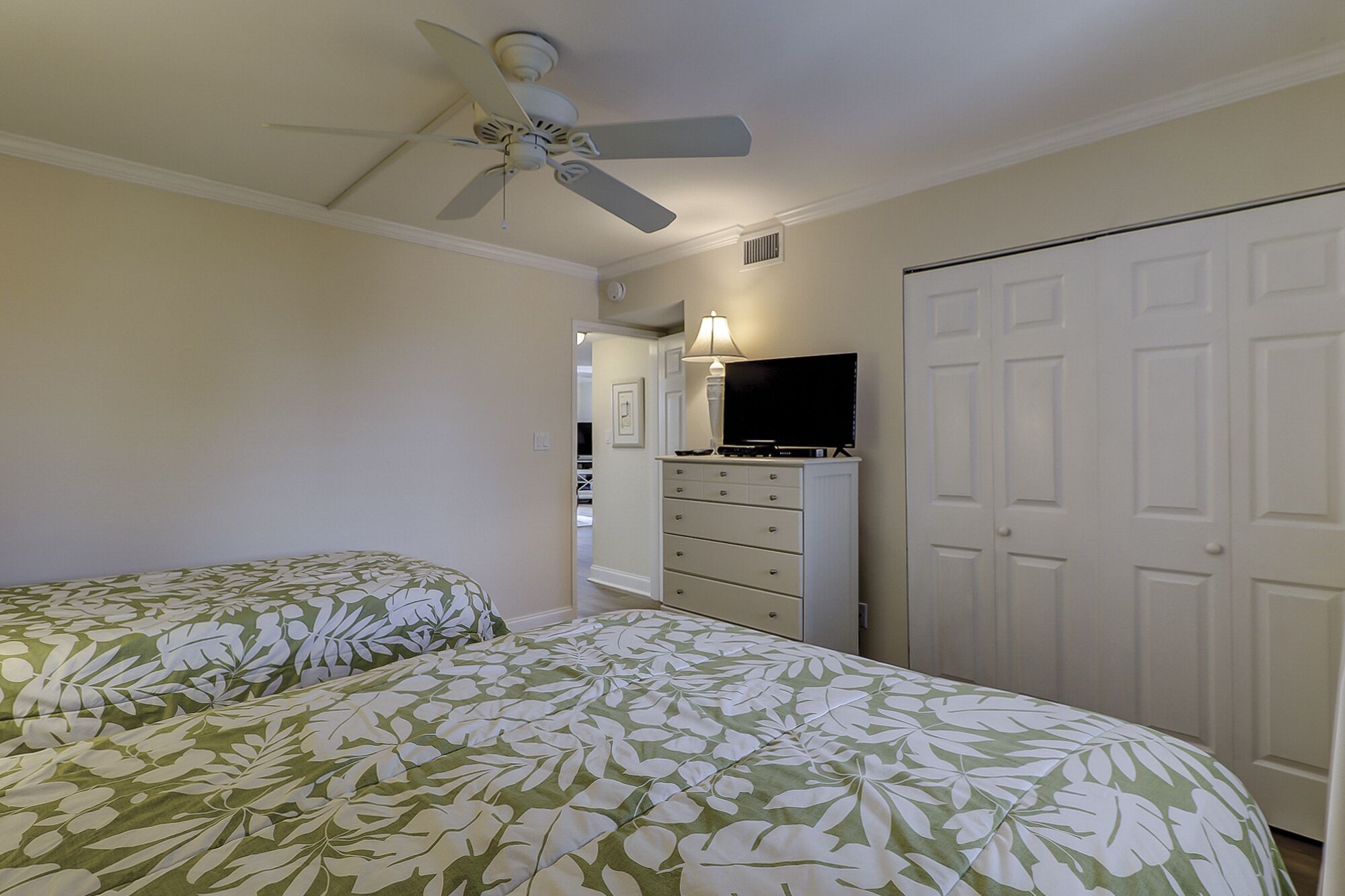 A bedroom with two beds, a ceiling fan, a dresser, a TV, and a closet.