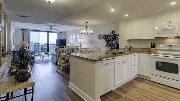 A modern kitchen with white cabinetry, a central island, and a dining area with a view. - 1501 Island Club - Folly Field - 2 Bed 2 Bath Sleeps 4 - Hilton Head Rentals (Hilton Head island)