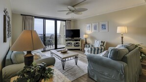 A living room with a sofa, armchairs, a coffee table, a TV, and a balcony with a view. - 1501 Island Club - Folly Field - 2 Bed 2 Bath Sleeps 4 - Hilton Head Rentals (Hilton Head island)