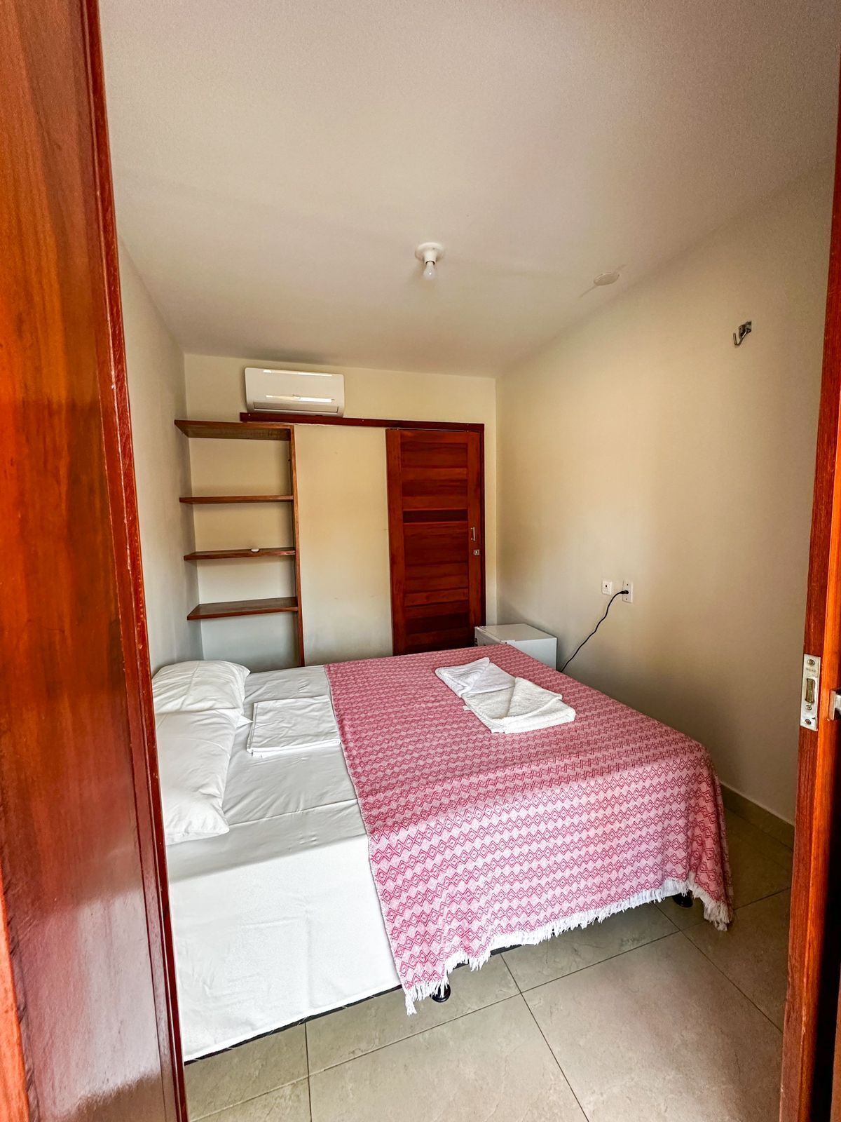 Une chambre à coucher comprenant un lit, une armoire en bois, une étagère et un climatiseur fixé au mur.