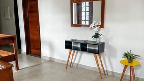 Un salon moderne avec une table à manger en bois, une console noire agrémentée d’un miroir et une petite table d’appoint jaune sur laquelle est posée une plante.