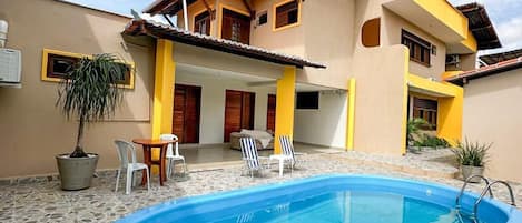 A two-story house with a swimming pool, outdoor furniture, and potted plants.