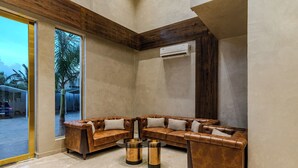 A modern living room with a sectional sofa, a coffee table, and an air conditioning unit. - Hotel Sannidhi Emerald (Yadagirigutta)
