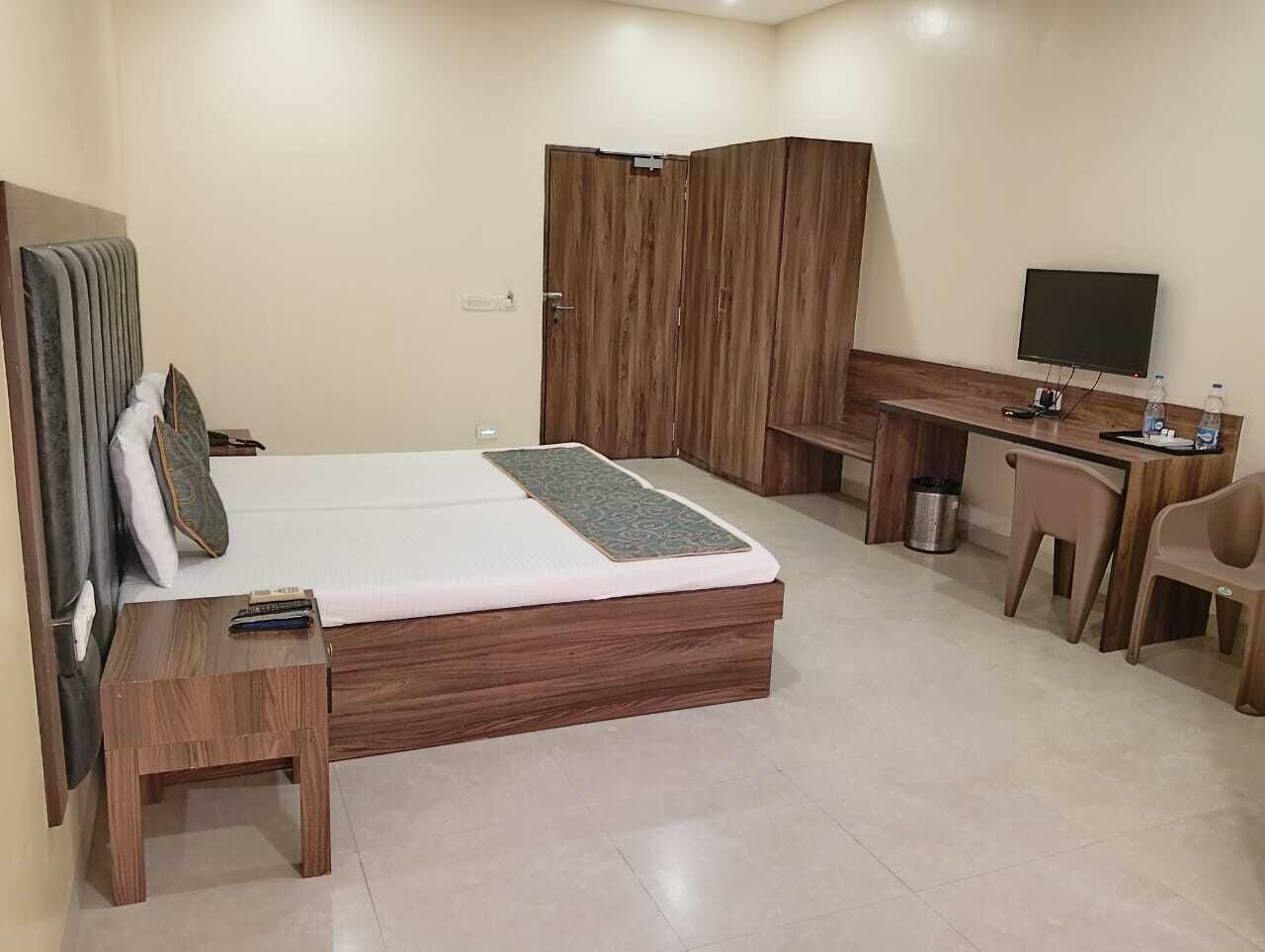 A hotel room with a bed, a desk, a chair, a TV, and a wardrobe.