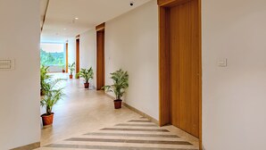 A hallway with wooden doors, potted plants, and a tiled floor. - Hotel Sannidhi Emerald (Yadagirigutta)