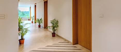 Un pasillo con puertas de madera, plantas en macetas y piso de baldosas.