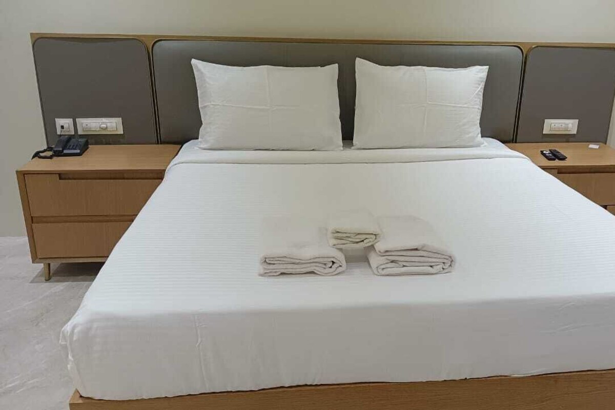 Un lit bien fait, avec des draps blancs, deux oreillers et des serviettes pliées posées sur le lit.